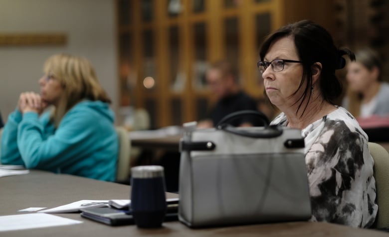 A woman with a serious expression on her face listens to a lecture in a classroom.