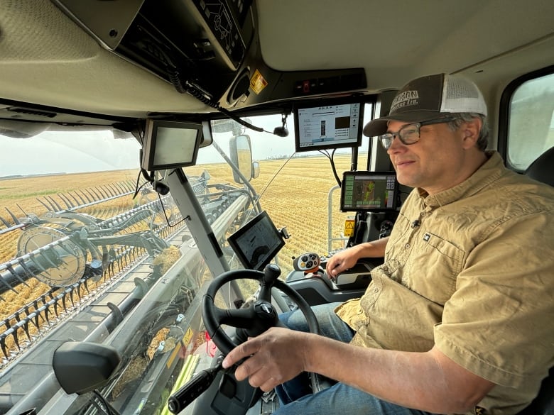 Ken Sarauer turning steering wheel inside cab of combine, with screens next to him