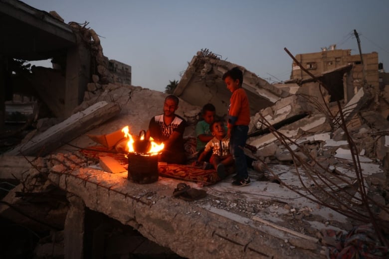 A man and three boys sit near a fire. 