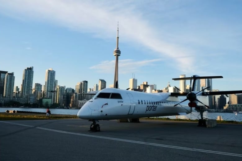 A white twin propeller aircraft sits on a tarmac with Toronto's CN tower in the background.