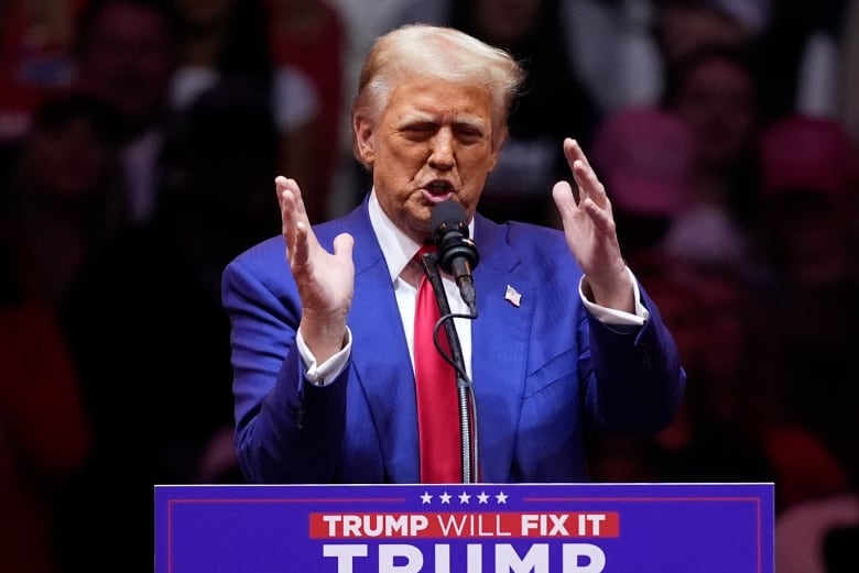 A person gestures while speaking into a lectern's microphone.