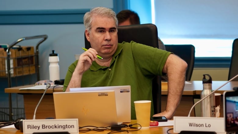 A man in a green polo shirt holds a green pen. 