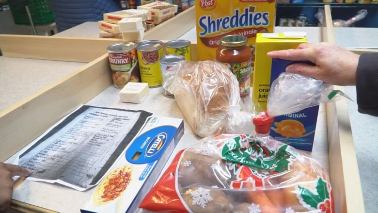 A hand lifts a box of Kraft Dinner from a counter, surrounded by various food items.