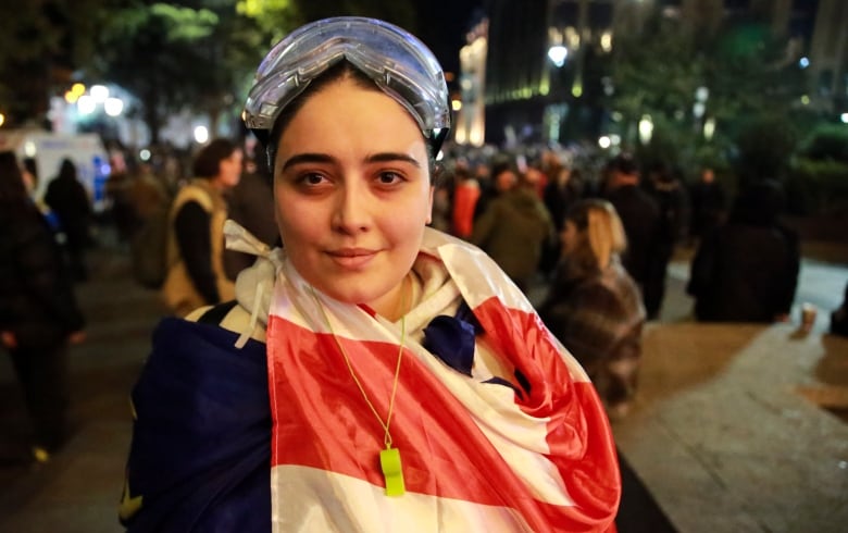 A young woman in a dark coat wears a red and white flag as a scarf.