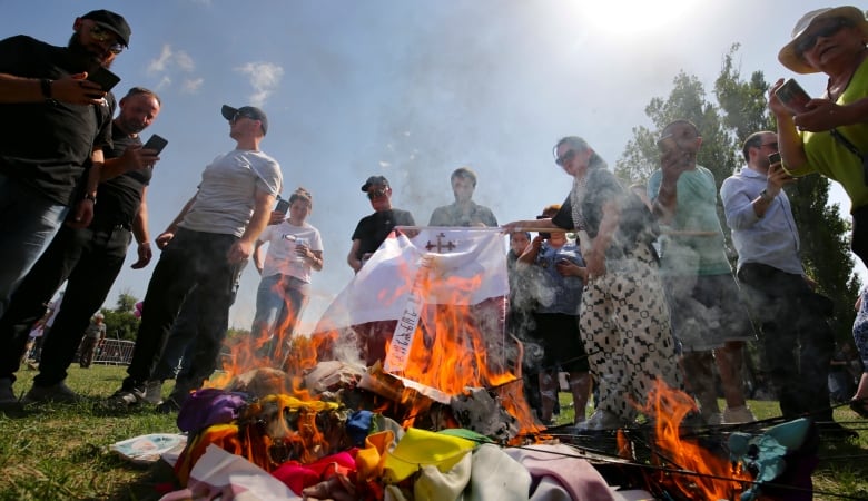 A group of people stand around a fire burning flags and other symbols.