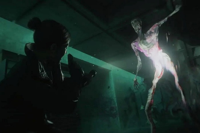 An image from a video game shows a person in a darkened room wielding a weapon, looking up at a glowing, spectral being with a scary face