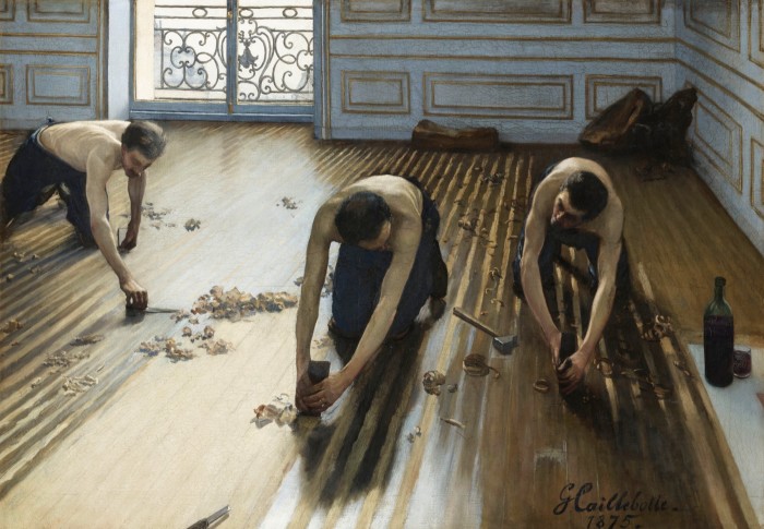 Three men stripped to the waist work on their knees at stripping the varnish of a wooden floor of a room with ornate panels 