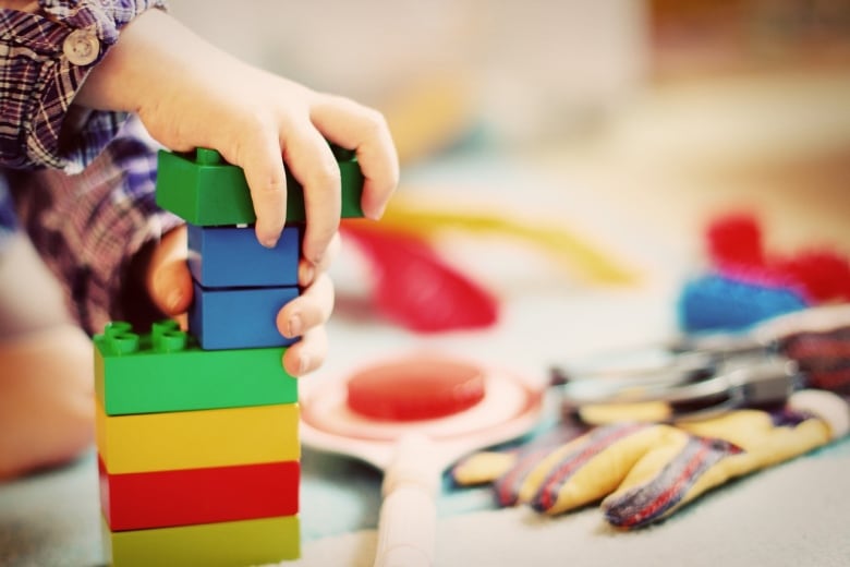 A child's hands can be seen playing with plastic building blocks.