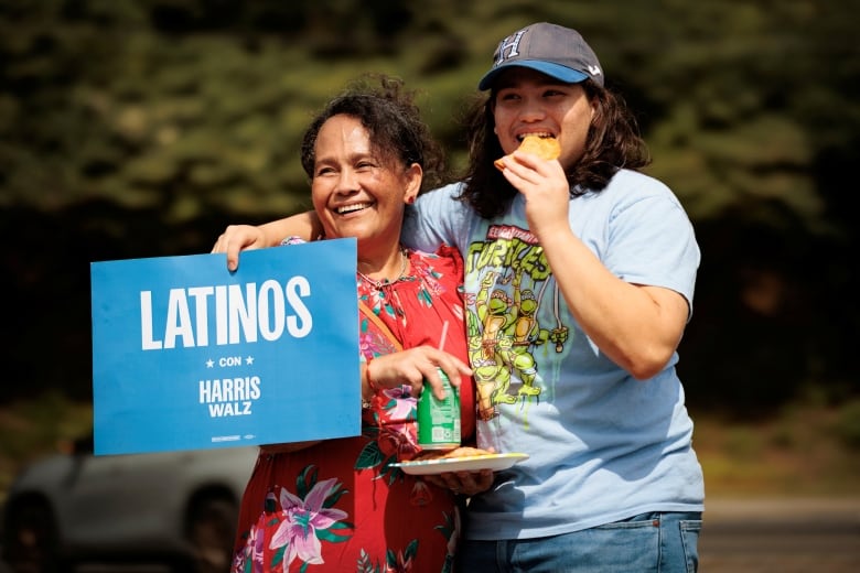 Two women hold a Latinos con Harris Walz" sign