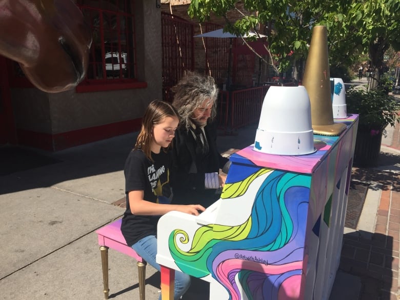 A man and a teenager play a piano outdoors.