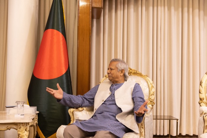 Yunus sits in front of a large Bangladesh flag