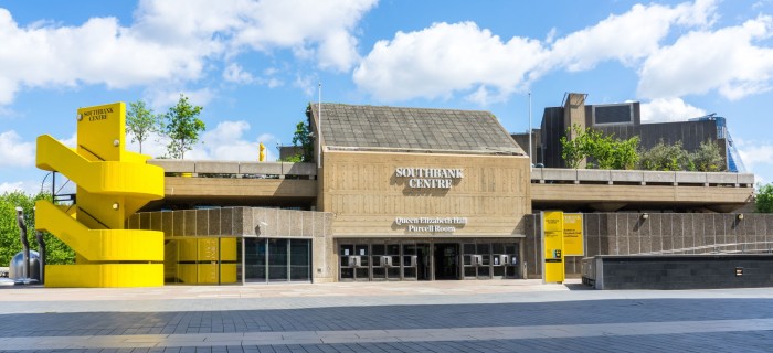 A building made from concrete, with glazed doors on the ground floor. To the left is a concrete spiral staircase, which has been painted bright yellow