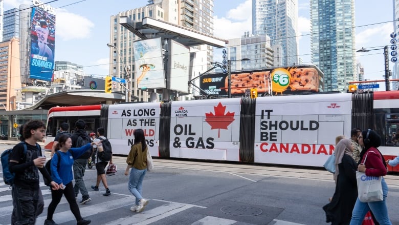 A streetcar passes through Toronto, covered in an ad that reads 'As long as the world needs oil and gas, it should be Canadian.'