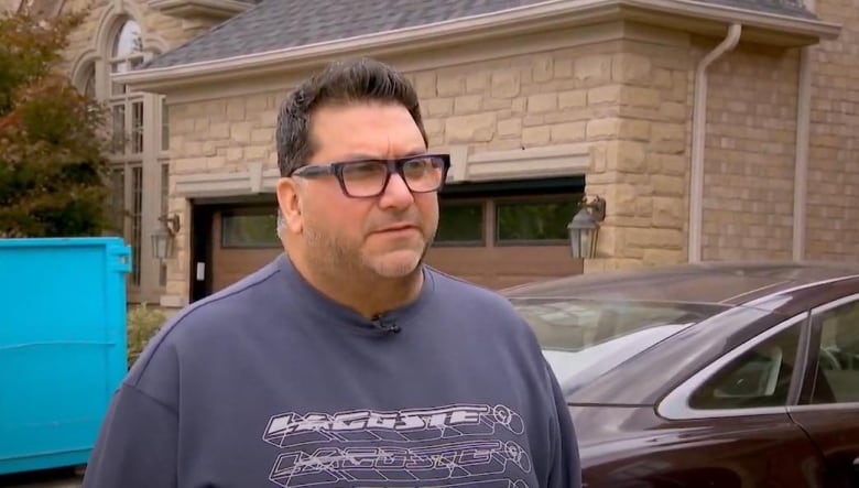 A man looks just off camera. He is standing in his front driveway.