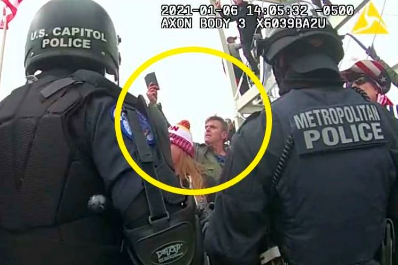 A large yellow circle highlights a person displayed in a still taken from video. In the still, the person is seen between two police officers. 