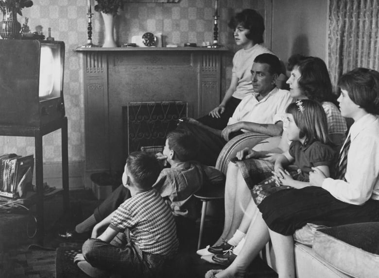 A black and white historical photo of a family watching television together at their home