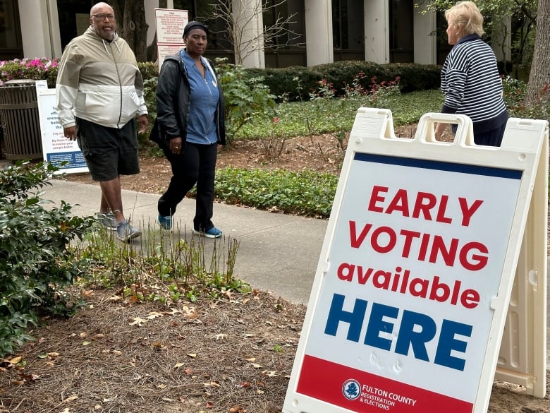 Three individuals are shown, walking in different directions, on a sidewalk near a sign that says 'Early Voting available here.'