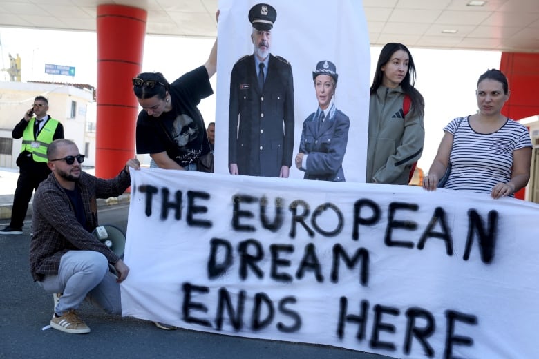 Four people stand in front of a white banner with black writing that reads: "The European Dream Ends Here."