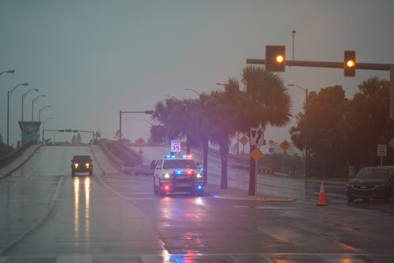 Two vehicles are shown on a roadway with their lights on, in a semi-darkened sky.