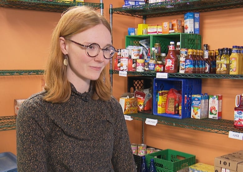 Woman standing in food bank with shelves of food behind her.