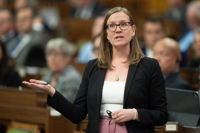 A woman in a black blazer and white shirt gestures with her hand as she speaks in the House of Commons.