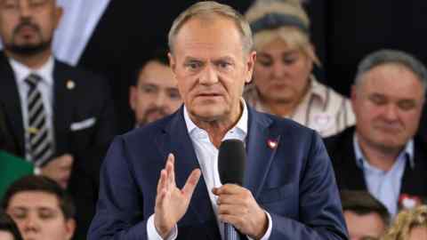 Donald Tusk speaks at the Civic Coalition convention in Warsaw, Poland. He holds a microphone, addressing the audience, with people seated in the background.