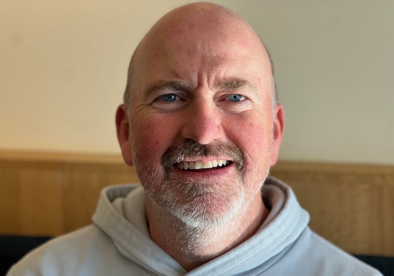 A bald man, with a grey goatee and wearing a grey hoodie, smiles.