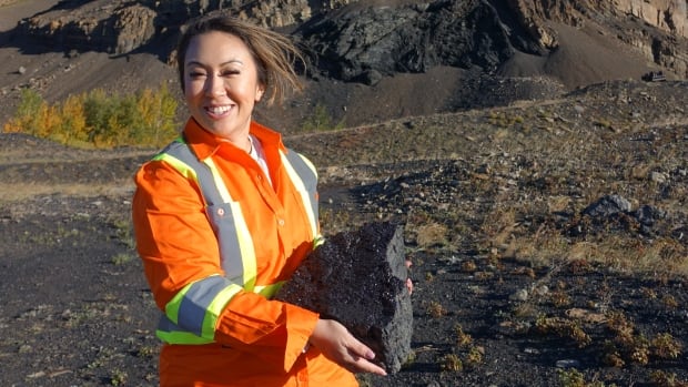 A woman in an orange safety jacket holds up a large piece of coal.