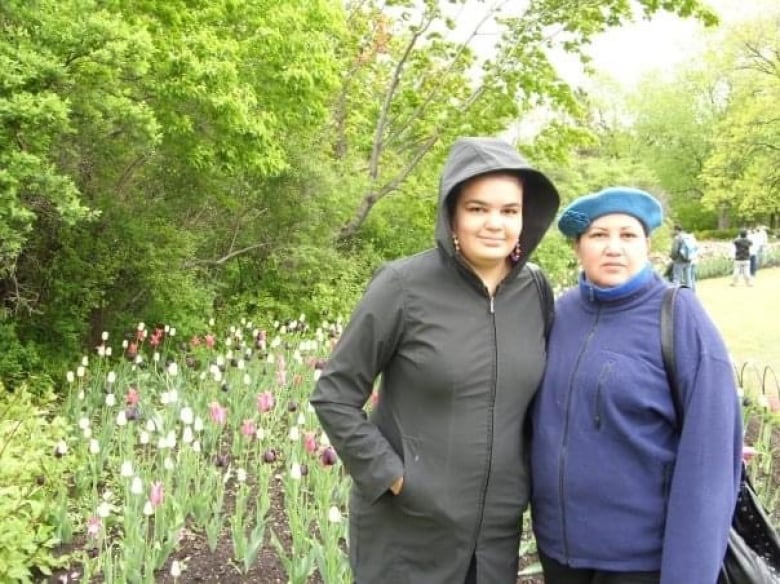 Two women posing for photo in front of tulips. They are wearing jackets. 