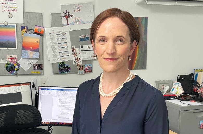 A woman in a business suit stands in front of a desk in an office.