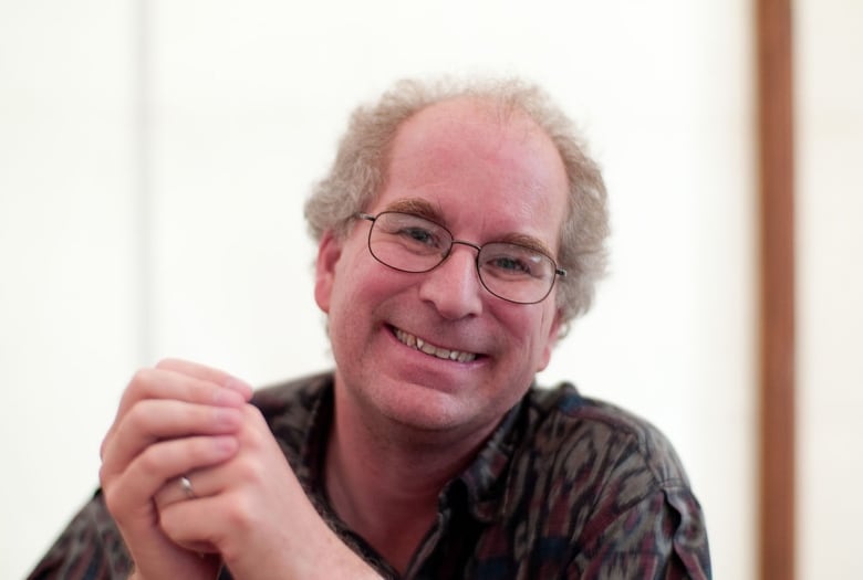 A man with glasses and white hair is smiling at the camera. 