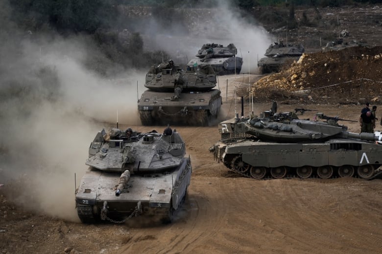 Four tanks are shown in a photograph, kicking up dust and dirt as they travel.