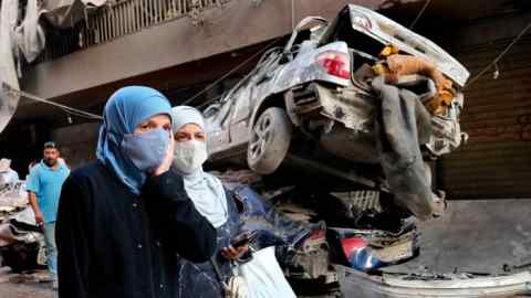 Lebanese women in Beirut pass destroyed cars after an Israeli air strike