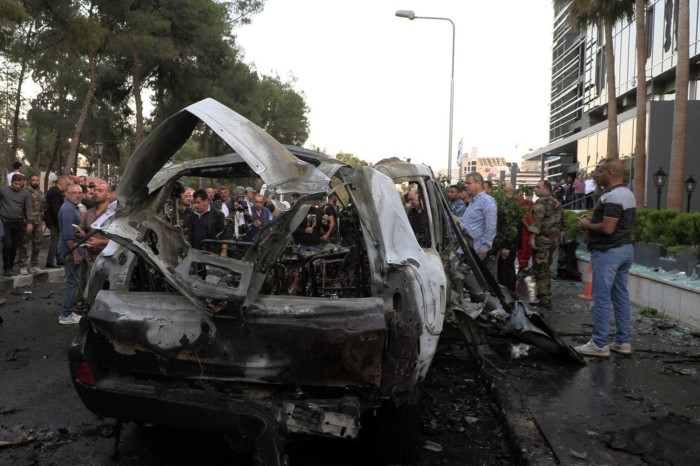 A crowd gathers around the  burnt-out remains of a vehicle targeted in an air strike in the Mazzeh area of Damascus on Monday