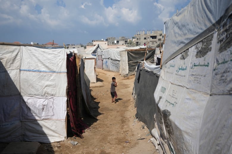 A displaced Palestinian boy carries bread as he walks between tents.