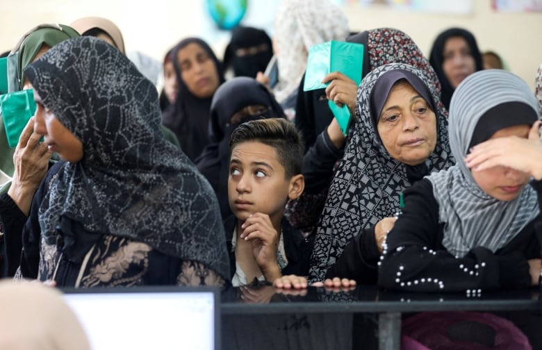 Several women wearing headcoverings and a young boy are shown crowded in a lineup.