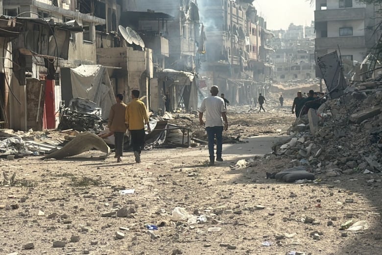 People walk past damaged and destroyed buildings.