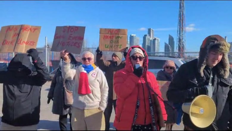 Men and women hold up signs protesting the living conditions in their apartments. One woman is speaking into a megaphone.