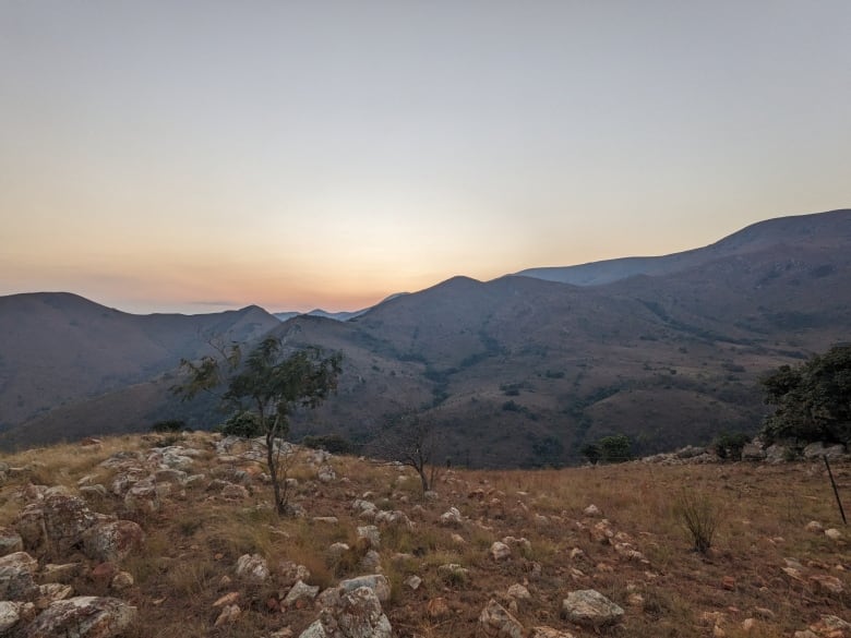 Rocky plains are seen in front of a hilly landscape and a dusty orange sunset.