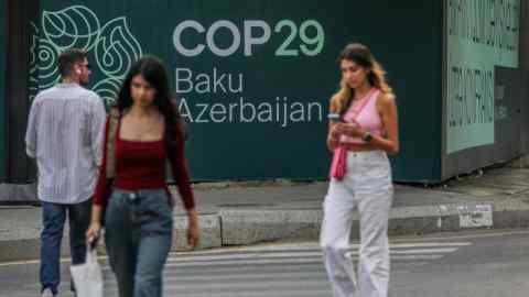 People walk past a large banner on a street promoting COP29 in Baku, Azerbaijan