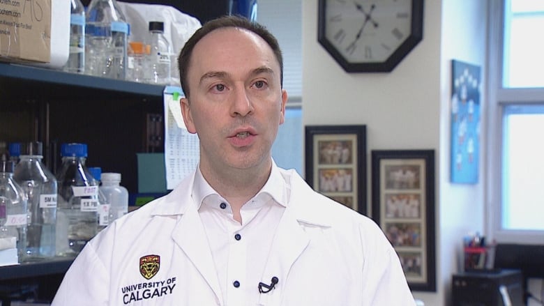 a man in a white lab coat that says university of calgary looks at the  camera