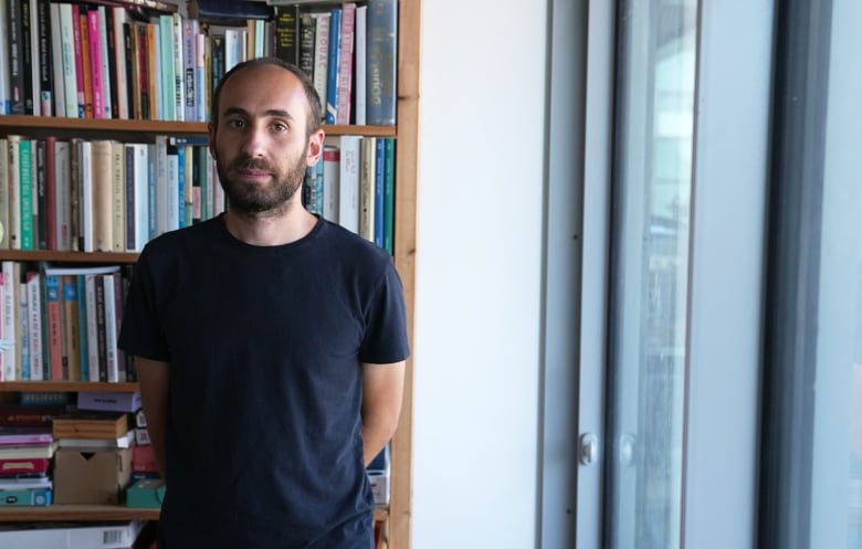 A man stands in a room with books behind him.