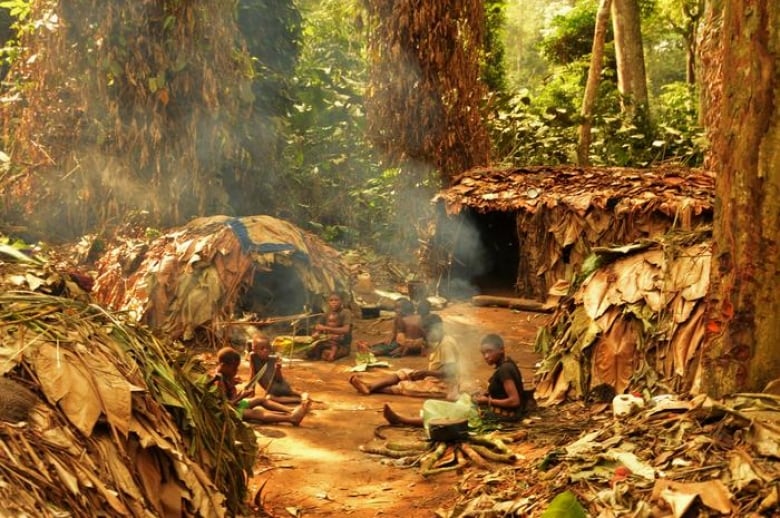 A photo of children sitting around huts in a rainforest