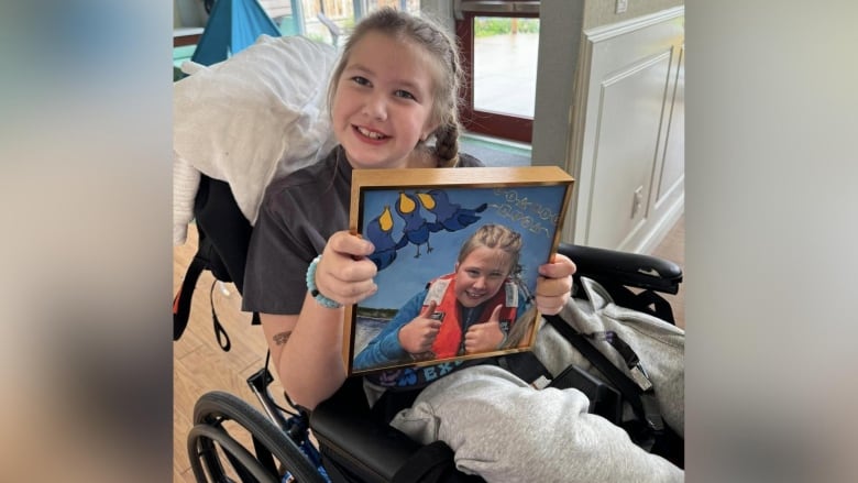 A girl in a wheelchair holds a picture of herself.