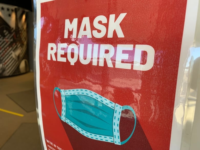 A large red sign shows a picture of a medical mask with the words 'MASK REQUIRED' printed in large bolded white lettering.