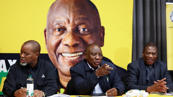 South Africa’s President Cyril Ramaphosa, centre, and deputy president Paul Mashatile, right, sitting in a meeting in front of a large image of Ramaphosa in June 2024