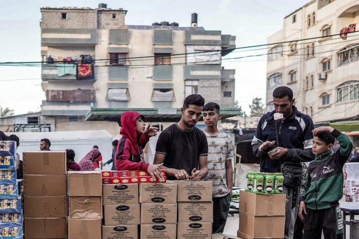 A vendor sells processed cheese and other packaged food products along a market street in Deir el-Balah