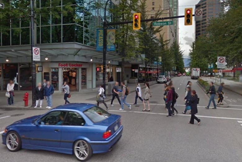 A downtown urban intersection on a cloudy day shows pedestrians in a crosswalk and vehicles in the background.