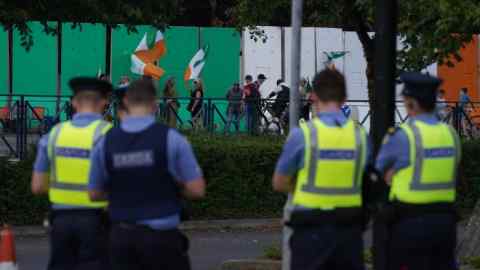 Garda officers watch protesters at the entrance to the site of the former Crown Paints factory in Coolock, north Dublin, recently painted in the colours of the Irish tricolour