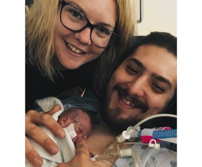 Smiling mother and father hold tiny premature baby in their arms.